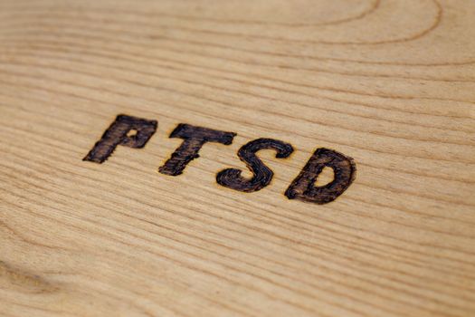An abbreviation PTSD - post traumatic stress disorder - burned by hand on flat wooden board in diagonal composition. Close-up with selective focus.