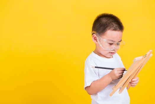 Asian Thai happy portrait cute little cheerful child boy smile are drawing on blackboard and looking the board, studio shot isolated on yellow background with copy space