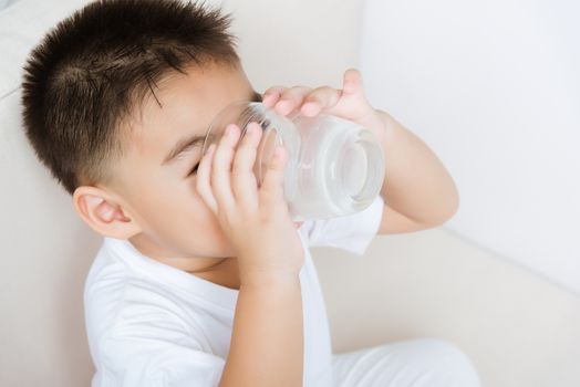 Close up of happy Asian little cute child boy hand holding milk glass he drinking white milk during sitting on the sofa at home after lunch. Daily life health care Medicine food