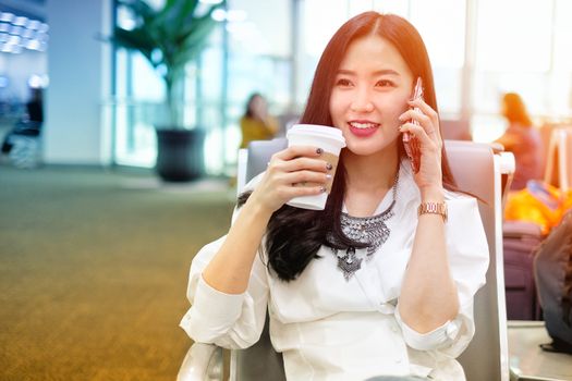 Woman drinking coffee and talking on the phone while waiting to board at the airport