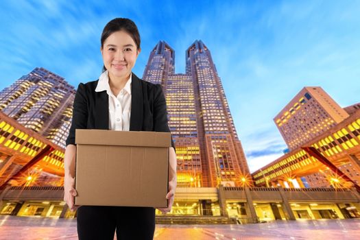 A young woman carrying a box wtih smile in night cityscape background

