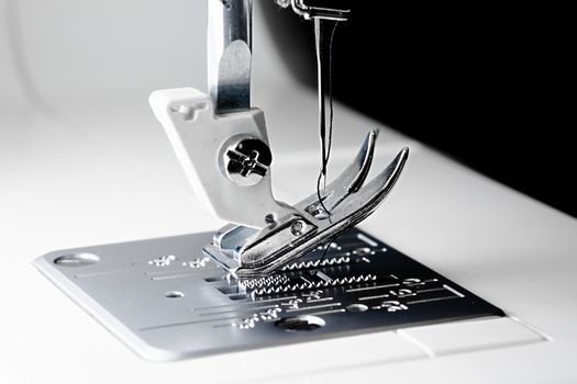 3 - Close macro sewing machine image with selective focus showing needle, thread, presser foot, feed dogs and throat plate.