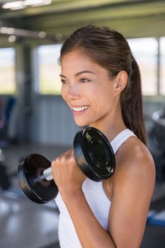 Asian woman strength training biceps with free weights at gym, lifting dumbbells for arm workout.