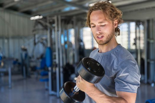 Man training biceps with free weights at fitness gym lifting dumbbells for arm workout.
