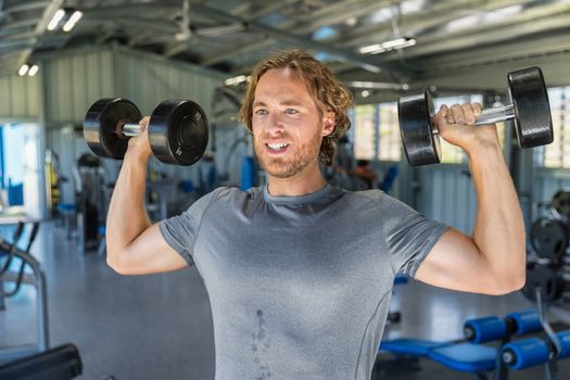 Fitness man doing military presses or standing dumbbell press exercise training in gym with free weights.