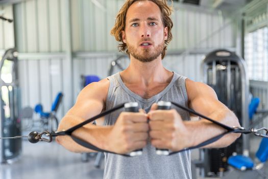 Man strength training in gym doing cable standing fly on tower.