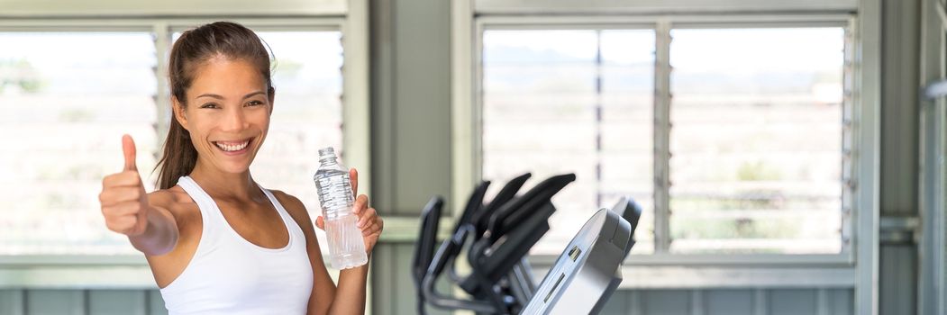 Happy girl drinking water bottle at fitness center banner panorama crop. Healthy woman doing thumbs up in gym training on running treadmill machine.
