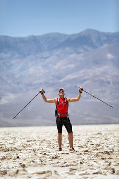 Hiker holding poles Cheering of Success against mountain. Full length of man in sports clothing on ultra running trail trek. Successful male is enjoying his vacation in Death Valley, USA travel.