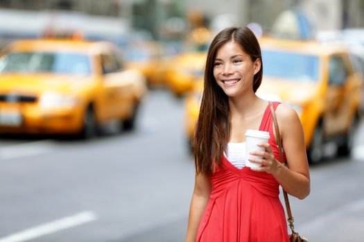 Smiling young woman holding disposable cup while walking on city street. Beautiful female is wearing red dress. Woman is with refreshing drink on street in city.