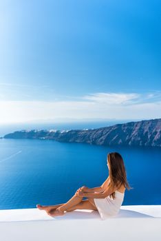 Luxury travel vacation Europe tourist woman relaxing at fancy hotel resort balcony in greek Santorini island, Greece with view over the Mediterranean Sea and Oia. Elegant girl living jetset lifestyle.