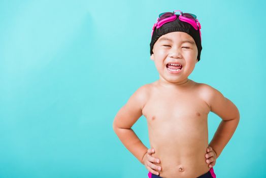 Summer vacation concept, Closeup portrait Asian happy cute little child boy wearing goggles and swimsuit, Kid having fun with in summer vacation looking camera, studio shot isolated blue background