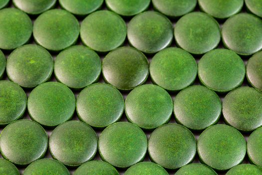 close-up background of many green organic spirulina tablets laid tight in one layer on flat surface.