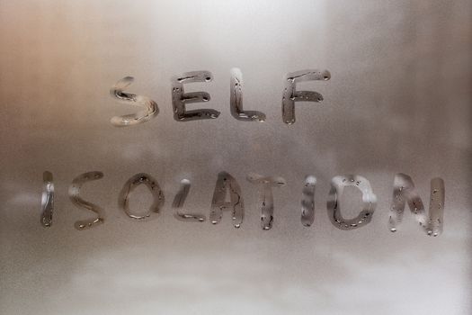 the words self isolation handwritten on wet window glass at daytime - close-up full frame picture with selective focus and background blur