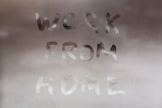 the words work from home handwritten on wet window glass at daytime - close-up full frame picture with selective focus and background blur