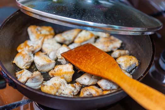 fried chicken in a open pan with ground black pepper and wooden kitchen spatula, closeup with selective focus