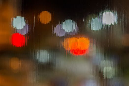 red and brown night lights bokeh trough wet glass close-up with selective focus abstract background