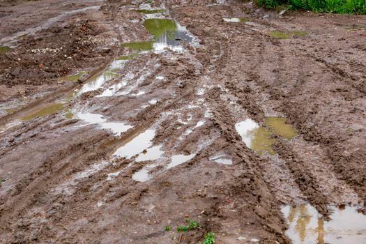 dirty clay mud crossroads with puddles and tire tracks - close-up with selective focus and linear perspective.