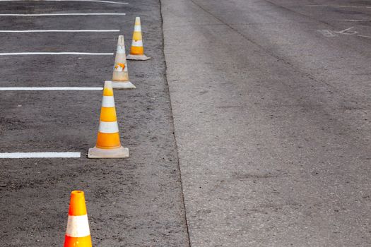 Orange road cones on a asphelt driving area with white lines, close-up with selective focus and backgropund blur.