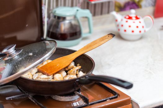fried chicken in a open pan with ground black pepper and wooden kitchen spatula, closeup with selective focus