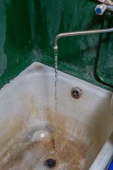 close view of old stained water tap and rusted bathtub with selective focus and blur.