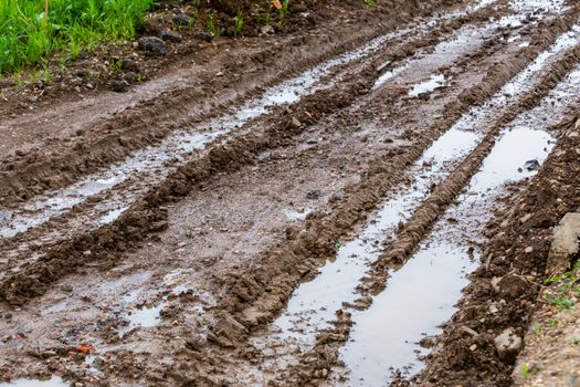 dirty clay mud road with puddles and tire tracks - closeup with selective focus and blur, diagonal composition