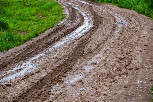 dirty clay mud road turn with puddles and tire tracks - closeup with selective focus and linear perspective.