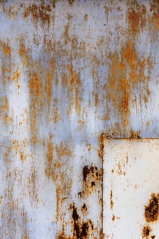 rusted flat solid sheet metal surface with leftovers of white and light blue paint, with rectangular patch in the corner, vertical orientation shot