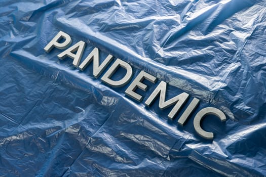 the word pandemic laid with silver letters on crumpled blue plastic film - diagonal perspective composition with selective focus and dramatic light