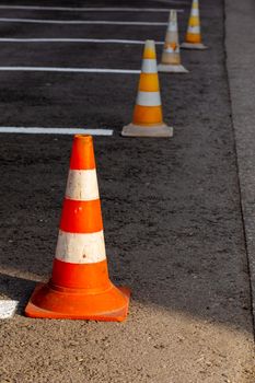 Orange road cones on a asphelt driving area with white lines, close-up with selective focus and backgropund blur.