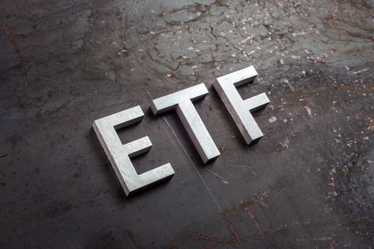the abbreviation word etf - Exchange Traded Fund - laid with silver letters on raw rusted steel sheet surface in slanted diagonal perspective.