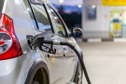 silver car refueling on night gas station - close-up with selective focus and blurry background.