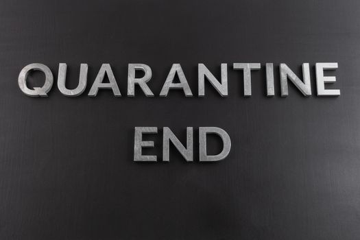 the words quarantine end laid with silver metal letters on matte back flat surface directly above in flat lay perspective, end of restrictions concept