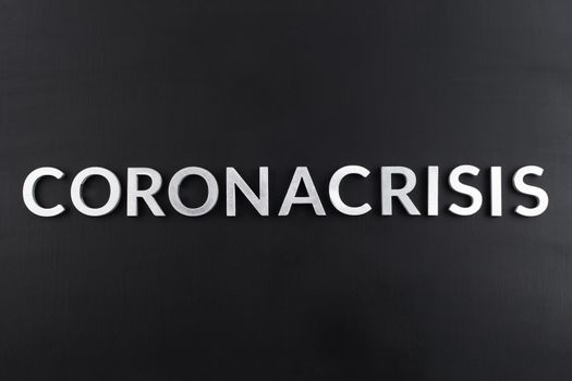 the word coronacrisis laid with white brushed metal letters on flat black surface in directly above perspective