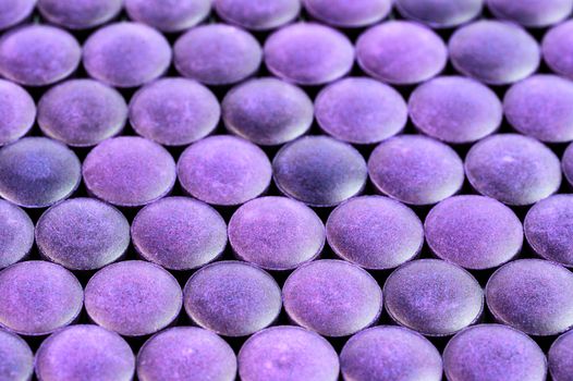 close-up background of many violet organic compacted powder tablets laid tight in one layer on flat surface.