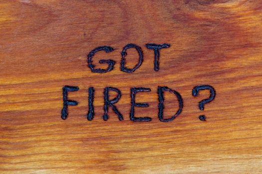 question got fired handwritten with hand woodburner on flat brown wood surface in flat lay directly above composition