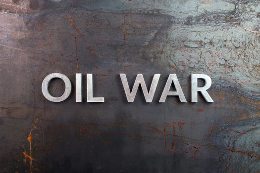 words oil war laid in line with silver metal letters on rusted heavy hot rolled uncoated steel sheet surface - directly above in flat lay composition