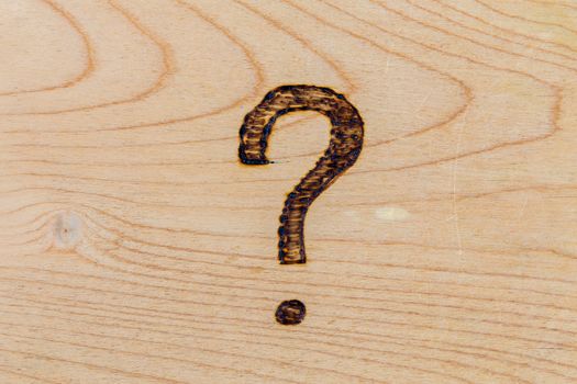 question mark drawn with handheld woodburner on bright flat wooden surface.