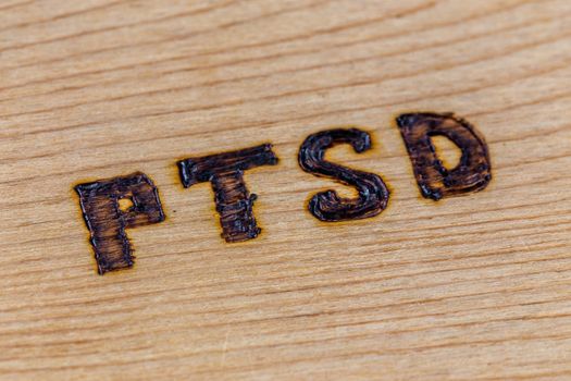 An abbreviation PTSD - post traumatic stress disorder - burned by hand on flat wooden board in diagonal composition. Close-up with selective focus.