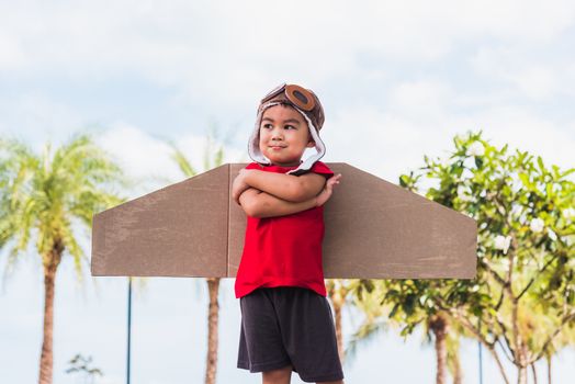Happy Asian funny child or kid little boy smile wear pilot hat and goggles play toy cardboard airplane wing fly stand crossed arm against summer sky cloud on garden background, Startup freedom concept