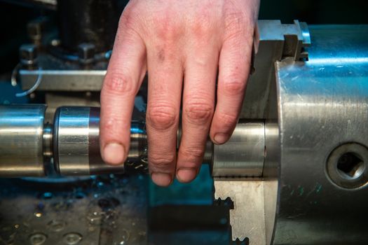 turner hand setting workpiece in 3-jaw chuck of small metalworking lathe - close-up with selective focus and background blur