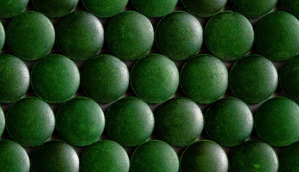 a seamless hexagonal pattern of many green organic spirulina tablets laid tight in one layer on flat surface.