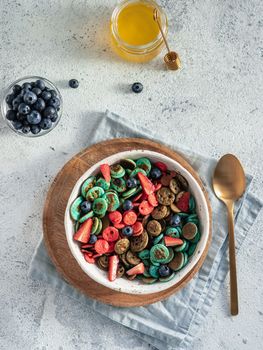 Trendy food - pancake cereal. Bowl of multi-colored mini cereal pancakes. Tiny pancakes with natural color - green matcha, turquose spirulina, blue pea, red fragon fruit. Top view or flat lay.Vertical