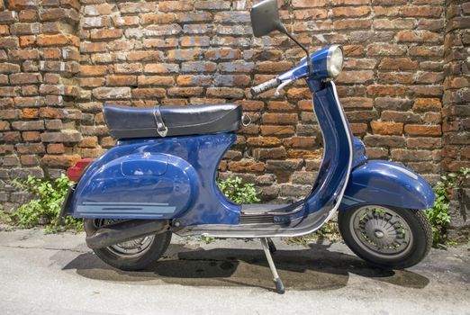 Vintage blue italian motorbike with brick ancient wall on background.