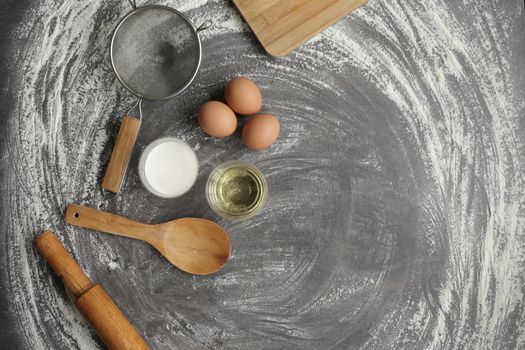 Chicken egg, flour, olive oil, milk, kitchen tool on gray table background. Products for baking bakery products. Cutting board, rolling pin, flour sieve, wooden spoon. For bread or cake
