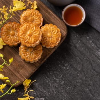 Mooncake, Moon cake for Mid-Autumn Festival, concept of traditional festive food on black slate table with tea and yellow flower, close up, copy space.