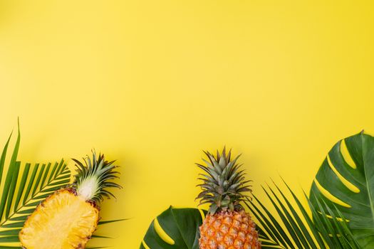 Beautiful pineapple on tropical palm monstera leaves isolated on bright pastel yellow background, top view, flat lay, overhead above summer fruit.