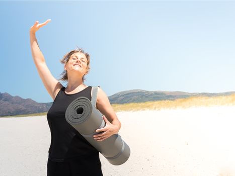 Woman in sportswear enjoying at the beach with a rolled-up mat under her arm . Copy space.