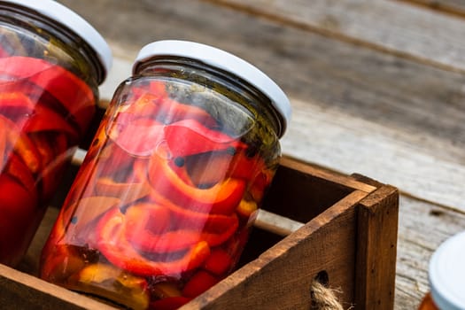 Wooden crate with glass jars with pickled red bell peppers.Preserved food concept, canned vegetables isolated in a rustic composition.