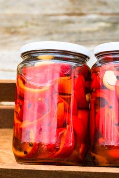 Wooden crate with glass jars with pickled red bell peppers.Preserved food concept, canned vegetables isolated in a rustic composition.