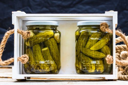 Wooden crate with glass jars with pickles isolated. Preserved food concept, canned vegetables isolated in a rustic composition.